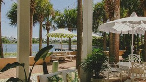Une terrasse extérieure avec des tables et des chaises blanches, des parasols et des plantes en pot.