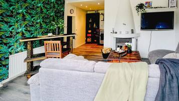 Un salon avec un canapé, une table basse, une cheminée, un téléviseur et un mur recouvert de plantes vertes.