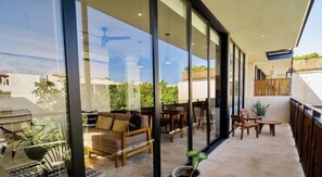 A modern outdoor living area with glass walls, a sofa, dining table, and chairs. - 2 Br. Spacious Great Located Top Amenities (Tulum)