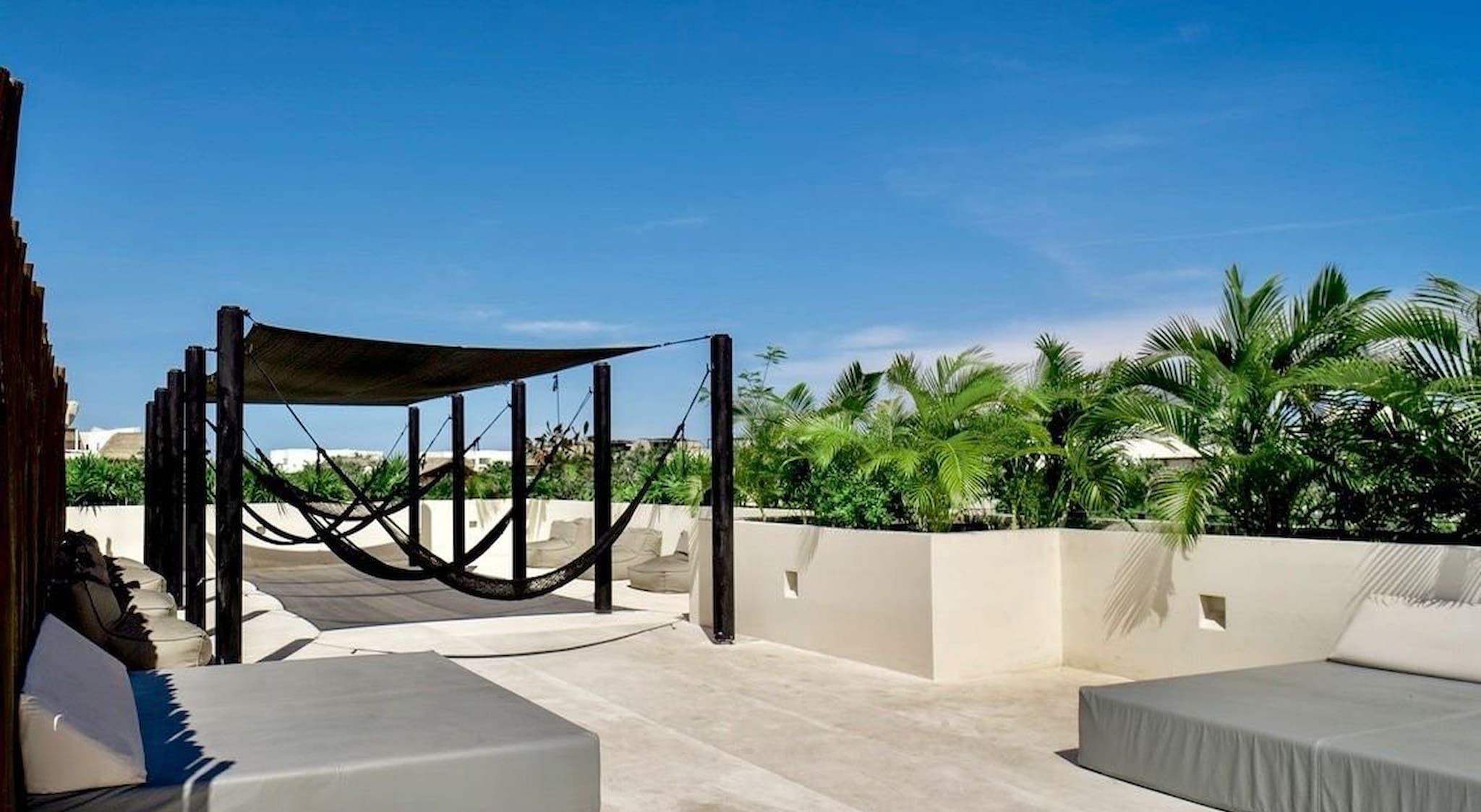 Una terrazza sul tetto con un'amaca, due zone relax grigie e vista su palme e edifici.
