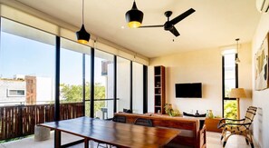 A spacious living area with a large wooden table, comfortable seating, a ceiling fan, and a TV mounted on the wall. - 2 Br. Spacious Great Located Top Amenities (Tulum)