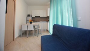 A compact living space with a kitchenette, a dining area, and a blue sofa. - Modern Two-room Apartment - Beahost (Rosolina)