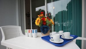 A white table with a blue tray holding white cups and saucers, a basket with colorful flowers, and a row of cups with colored stripes. - Modern Two-room Apartment - Beahost (Rosolina)