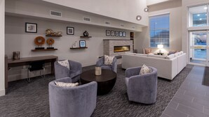 A modern living room with a fireplace, grey sofas, a coffee table, and a desk with a chair. - GrandStay Hotel & Suites Algona IA (Algona)