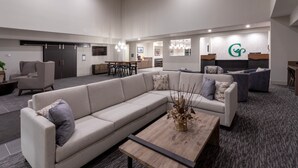 A modern lobby with a large L-shaped sectional sofa, a coffee table, and a reception desk with a logo. - GrandStay Hotel & Suites Algona IA (Algona)