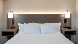 A hotel room with a large bed, two bedside tables, and wall-mounted lamps. - GrandStay Hotel & Suites Algona IA (Algona)