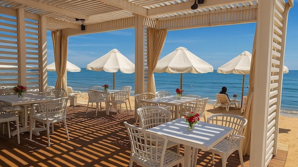 An outdoor seating area with tables and chairs, white umbrellas, and a view of the sea. - Simple & Serene Chalet (Port Said)
