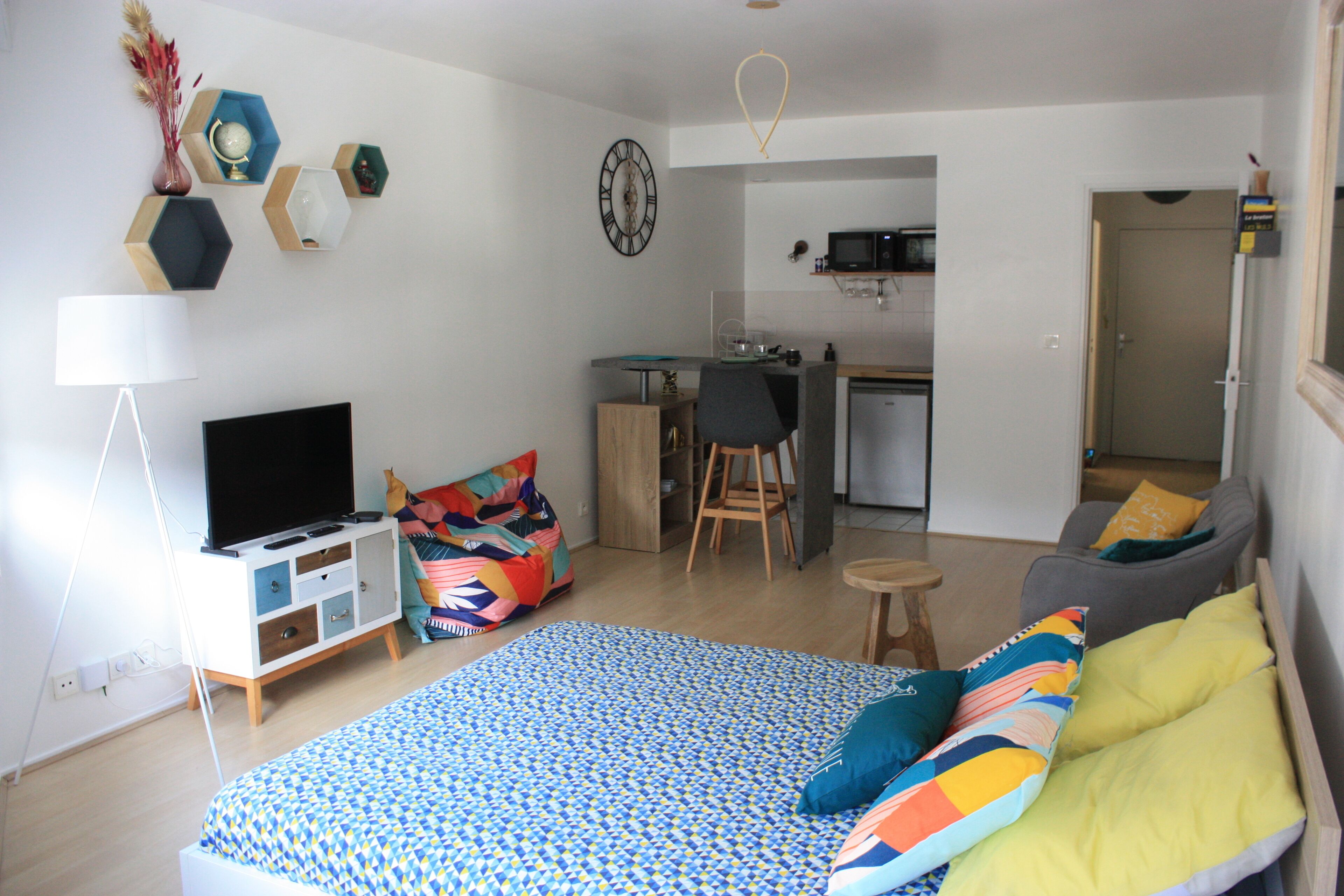 A compact living space with a bed, a TV, a desk, and a kitchenette.