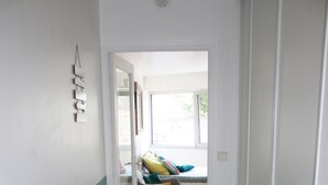 A hallway with a wooden floor, a door leading to a room with a bed and colorful pillows. - Studio de 33 m² en Centre-ville (Saint-Brieuc)