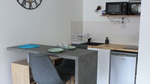 A compact kitchen with a central island, bar stools, a wall-mounted clock, and a microwave on a shelf. - Studio de 33 m² en Centre-ville (Saint-Brieuc)