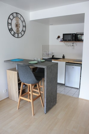 Una cocina compacta con una isla central, taburetes de bar, un reloj en la pared y un microondas en un estante.