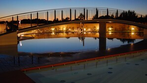 A bridge over a reflective pool with a railing and lights, surrounded by trees. - Stunning Apartment in a Holiday Village With Pool (San Michele al Tagliamento)