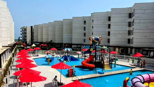 Una piscina con toboganes y zona de juegos acuáticos, rodeada de sombrillas rojas y sillas blancas.