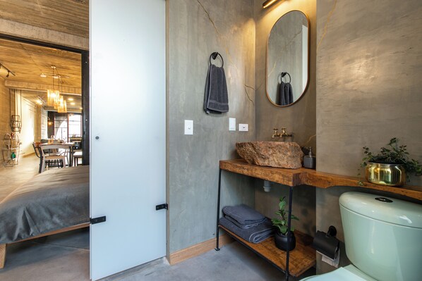 Une salle de bain moderne avec un grand miroir, une étagère en bois sur laquelle repose un rocher, et des toilettes.
