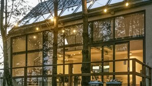 A modern building with large windows and a glass roof, surrounded by trees.