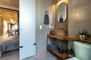 A modern bathroom with a large mirror, a wooden shelf with a rock, and a toilet.