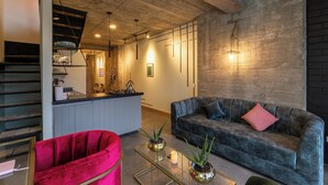 Un espacio de sala moderno con un sofá gris, una silla roja y una encimera de cocina con un lavamanos.
