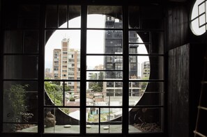 Blick durch ein rundes Fenster mit Gittermuster auf eine Stadtlandschaft mit verschiedenen Gebäuden.