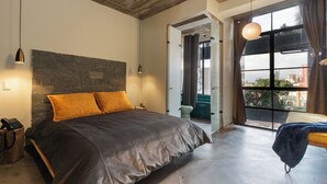 Une chambre à coucher moderne avec un grand lit, un mur en pierre et une vue sur la ville, visible à travers une grande fenêtre.