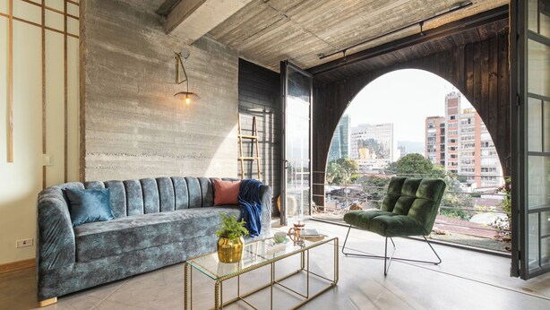 Un salon moderne avec un canapé, une table basse en verre et une vue sur la ville, visible à travers une fenêtre en arc de cercle.