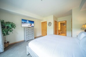A hotel room with a large bed, a dresser, a television mounted on the wall, and a potted plant. - Gateway Lodge 5015 (Keystone)