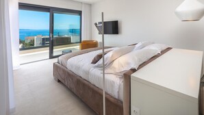 A modern bedroom with a large bed, a TV mounted on the wall, and a balcony with a view of the sea. - Stunning home in Lun with sauna (Lun)