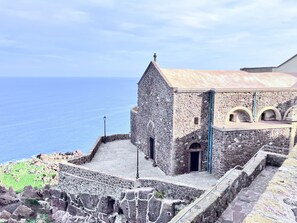 A stone building with a metal roof, a small entrance, and a view of the sea. - New Apartment Nomina Castelsardo (Castelsardo)
