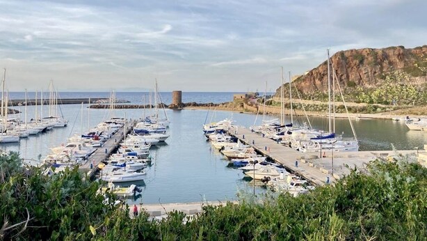Un port de plaisance où sont amarrés de nombreux bateaux, un ciel dégagé et une falaise rocheuse en arrière-plan.