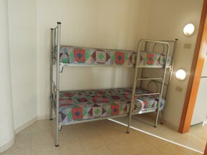 A bunk bed with a colorful quilt, metal frame, and a white wall with a light switch.