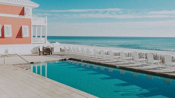 Una piscina con vista al océano, un edificio con balcón y una cerca a la orilla del agua.