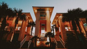 Un hotel con una escalera central, palmeras y un cartel que indica que es un club de playa.