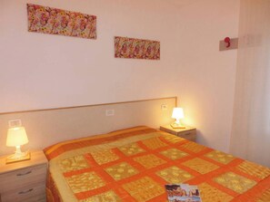 A bedroom with a bed, two bedside tables with lamps, and two floral wall decorations. - Cozy Villa Steps From the Beach (San Michele al Tagliamento)