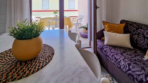 A living room with a sofa, a dining table with a plant, and a view of the outside balcony. - Modern and Comfy Flat Near the sea (San Michele al Tagliamento)