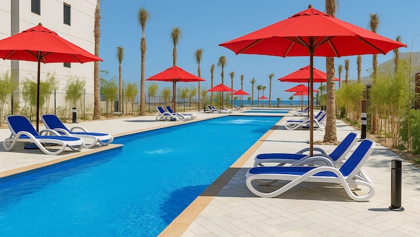A swimming pool with blue water, surrounded by lounge chairs and red umbrellas. - Unwind by the Coast at Porto Said Chalets (Al-Manasrah)