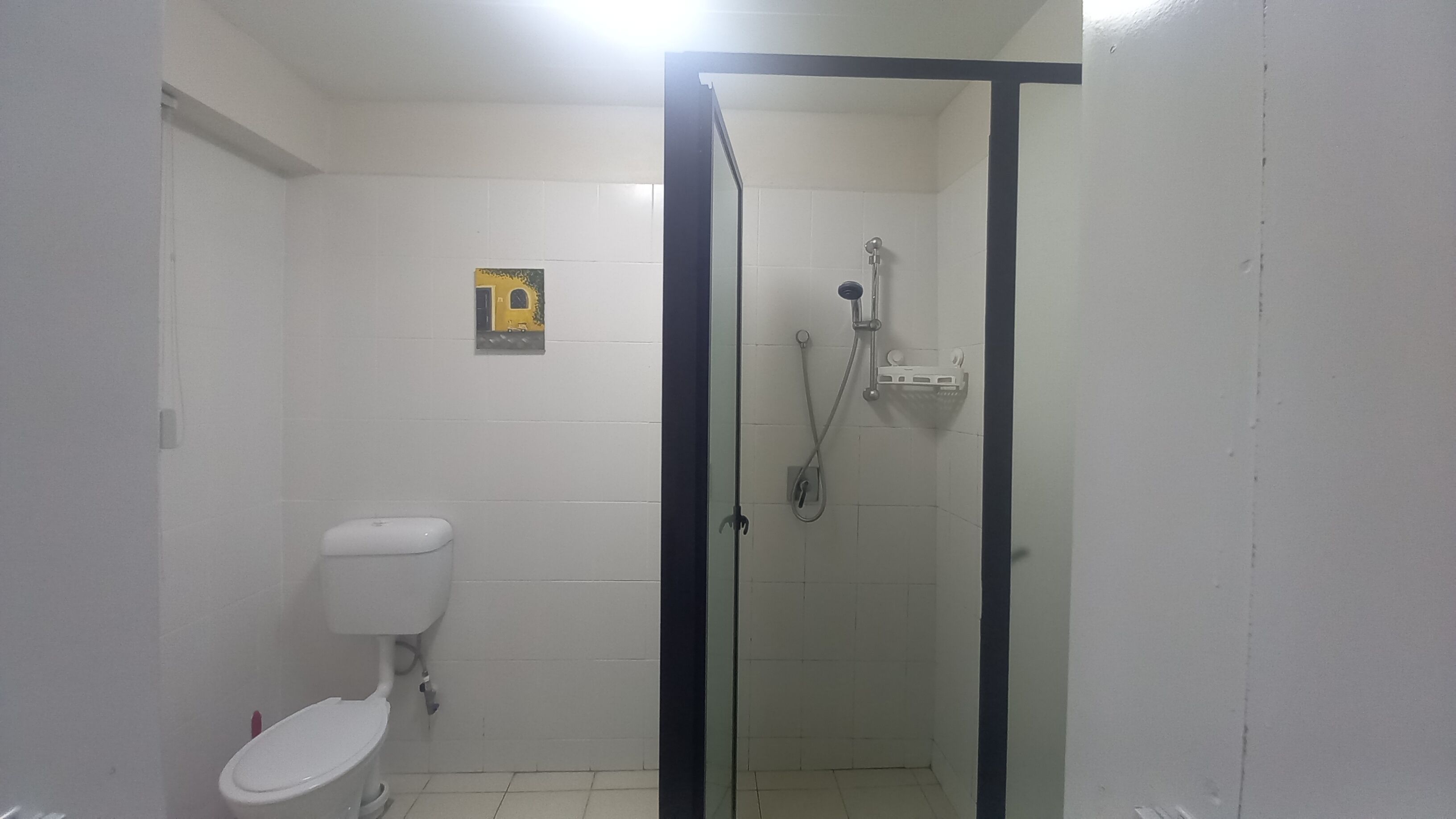 Een kleine, afgesloten douchecel met een glazen deur, een toilet en een handdroger aan de muur.