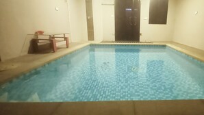 Una piscina techada rectangular con piso de baldosas y una puerta oscura al fondo.