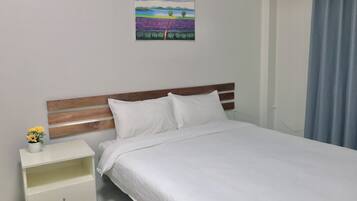 Una cama bien hecha con ropa blanca, un cabecero de madera y una mesita de noche con un florero de girasoles.