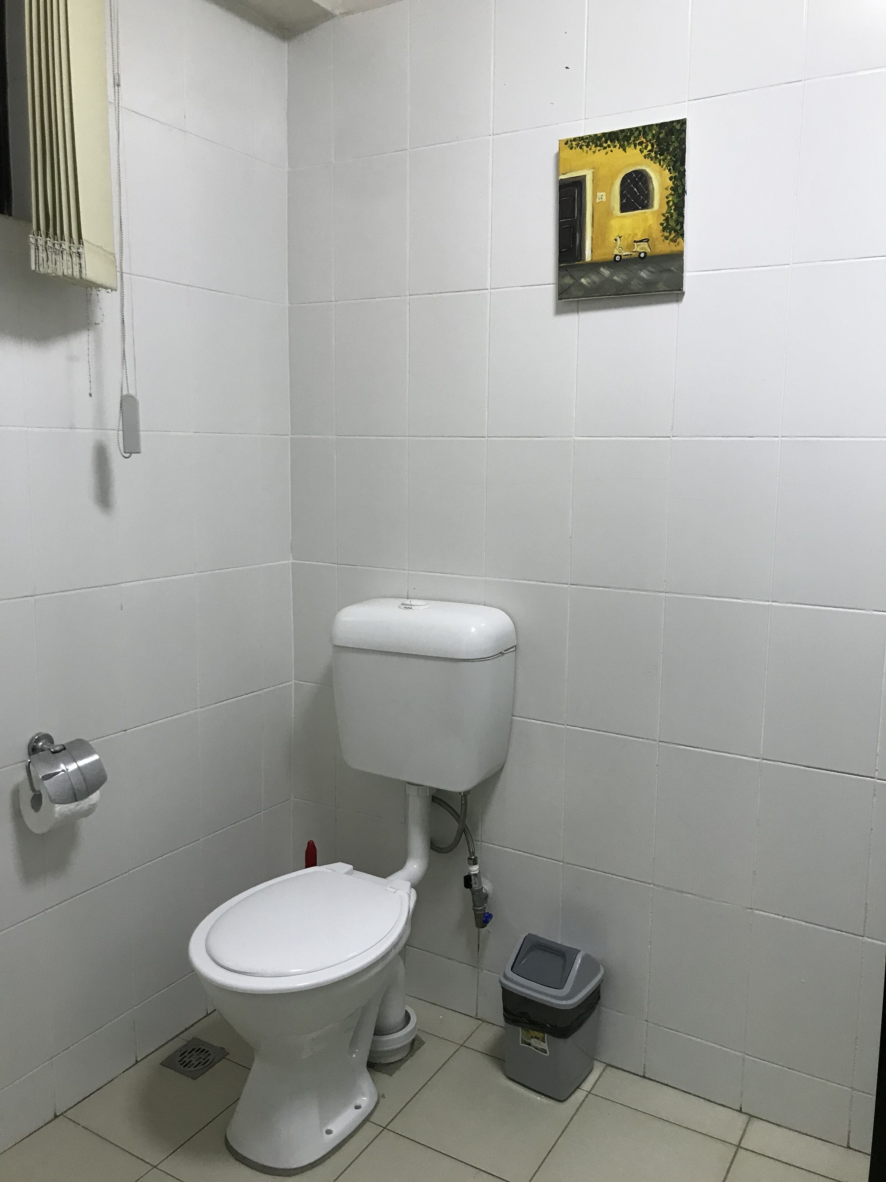 Une salle de bain standard équipée de toilettes, d’une poubelle et d’un porte-rouleau de papier toilette fixé au mur.