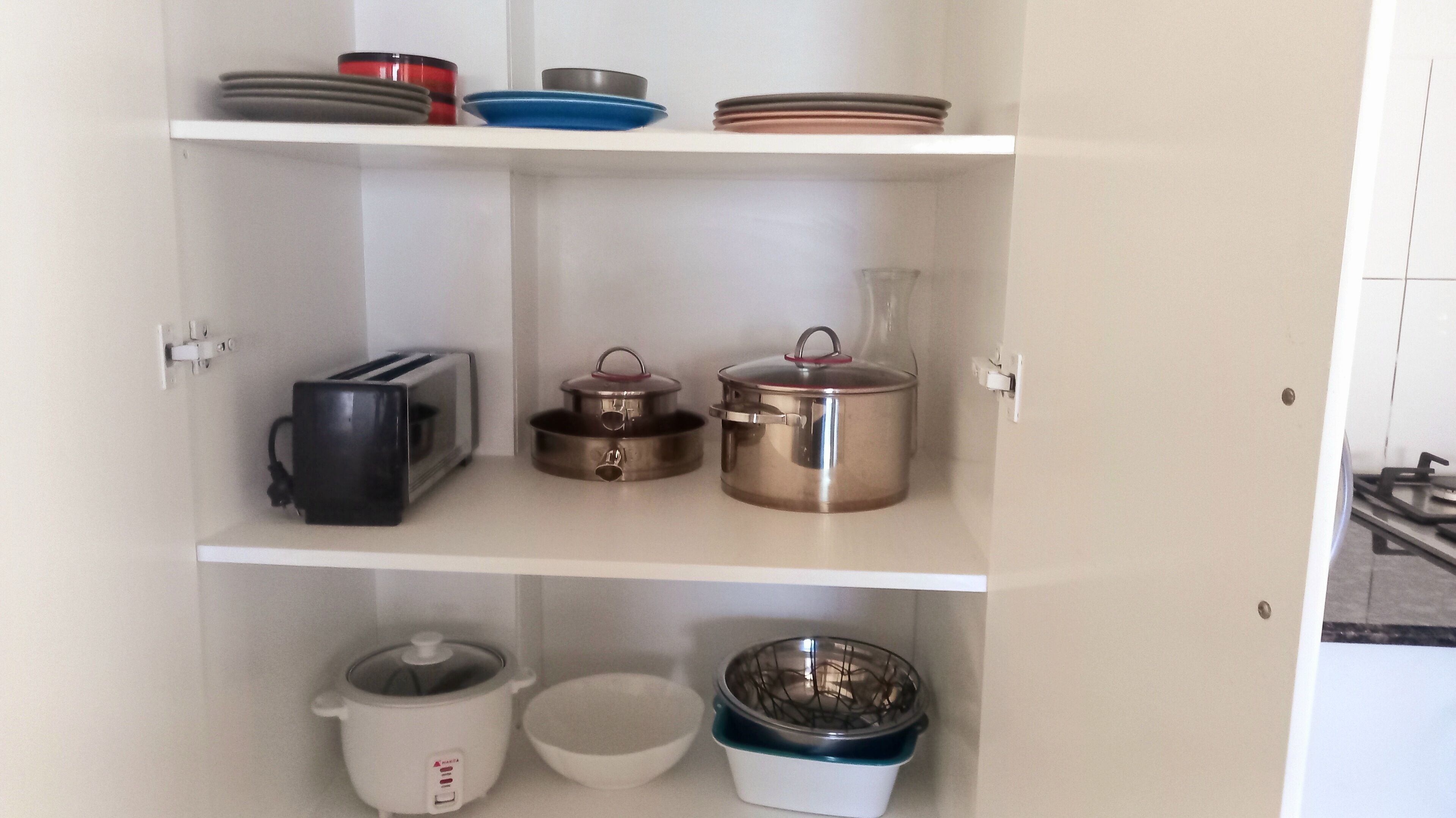 A kitchen with white cabinets, a toaster, a slow cooker, pots, and a bowl.