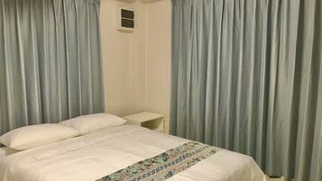 A bedroom with a bed, curtains, a nightstand, and a wall-mounted air conditioning unit.
