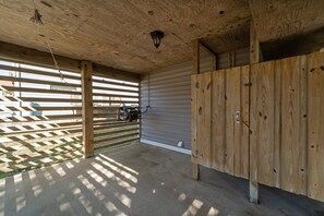Área externa coberta com piso de concreto, vigas de madeira e porta de garagem de metal.