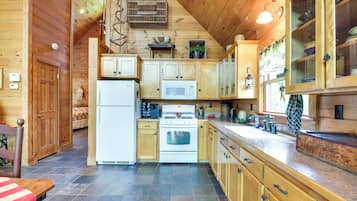L’intérieur d’un chalet en bois comprend une cuisine équipée d’un réfrigérateur, d’une cuisinière, d’un four à micro-ondes et d’armoires en bois.