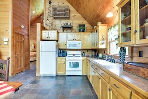 A wooden cabin interior with a kitchen featuring a refrigerator, stove, microwave, and wooden cabinets.