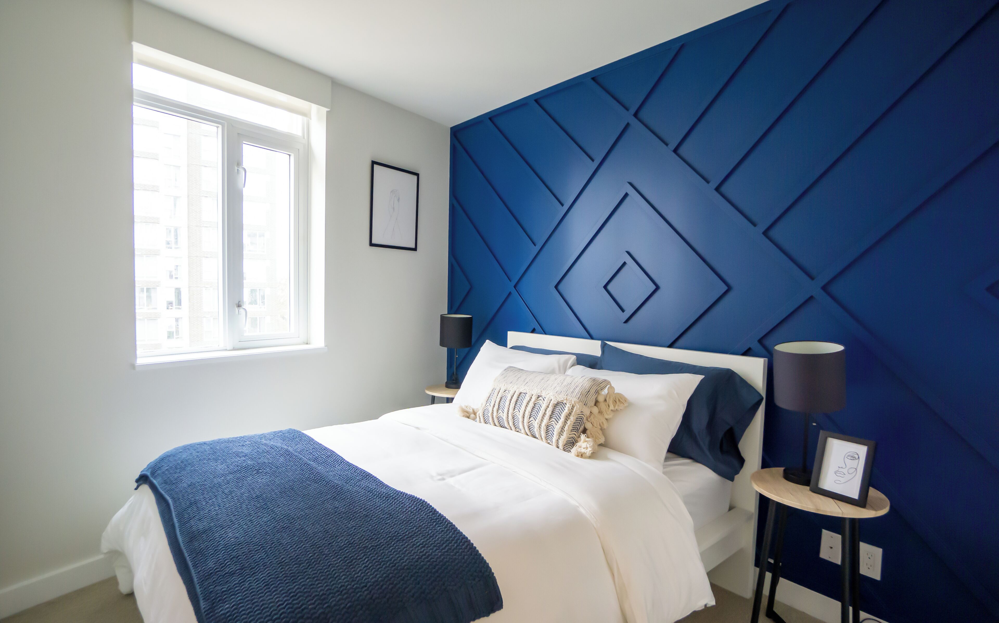 Een moderne slaapkamer met een blauwe accentmuur met geometrische patronen, een groot raam en een netjes opgemaakt bed.
