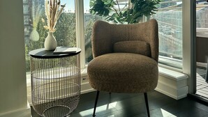 A room with a large window, a round metal table with a vase, and a plush chair.