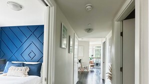 A modern hotel corridor with a dark wooden floor, white walls, and a blue accent wall in the bedroom area.