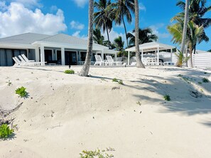 Une propriété située en bord de mer, dotée d’un espace extérieur aménagé avec une terrasse couverte, de palmiers et d’un paysage sablonneux.