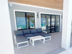 Un espace extérieur moderne aménagé avec un canapé et une table, de grandes portes vitrées donnant sur une zone autour de la piscine, et une vue sur l’océan.