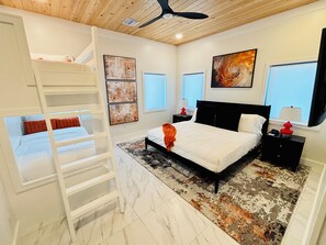 Une chambre avec un lit superposé, un grand lit, un ventilateur de plafond et des œuvres d’art accrochées aux murs.
