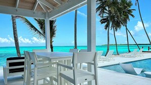 A covered outdoor area with a pool, white furniture, and palm trees.